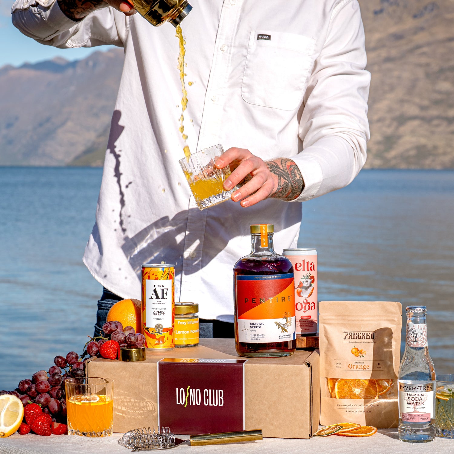 A LONO Club cocktail being poured into a glass at the lakeside with a LONO box and it's contents in front